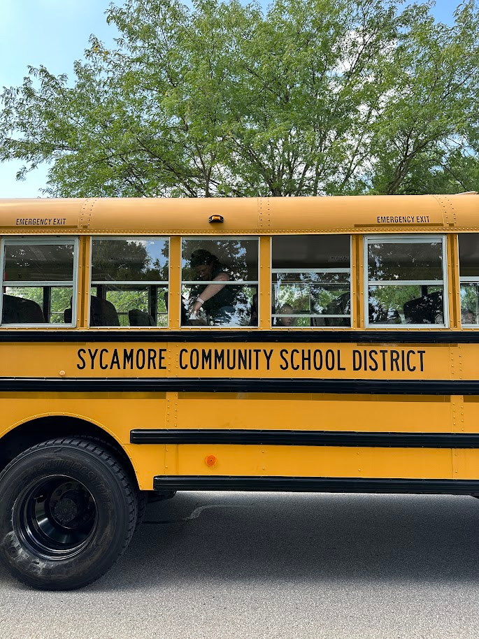 Photo: An aide straps a preschooler into a seat on a yellow school bus marked Sycamore Community School District.